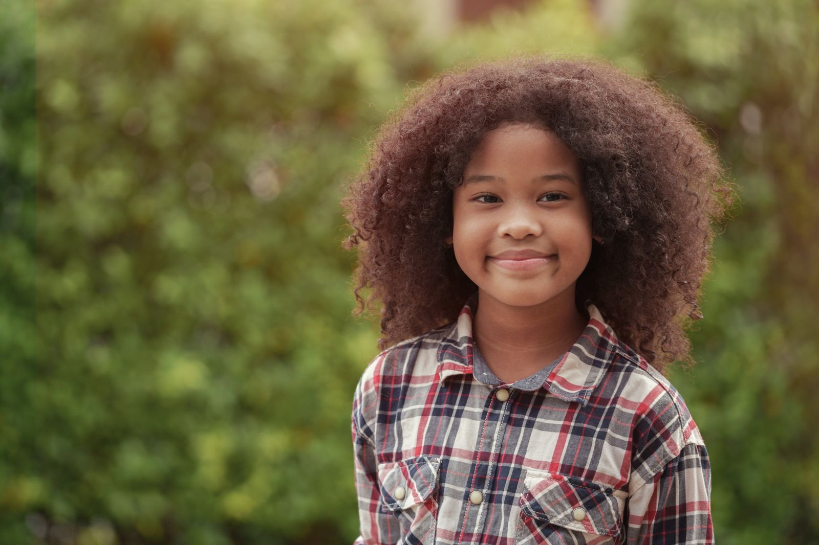 A smiling girl with curly hair in a plaid shirt