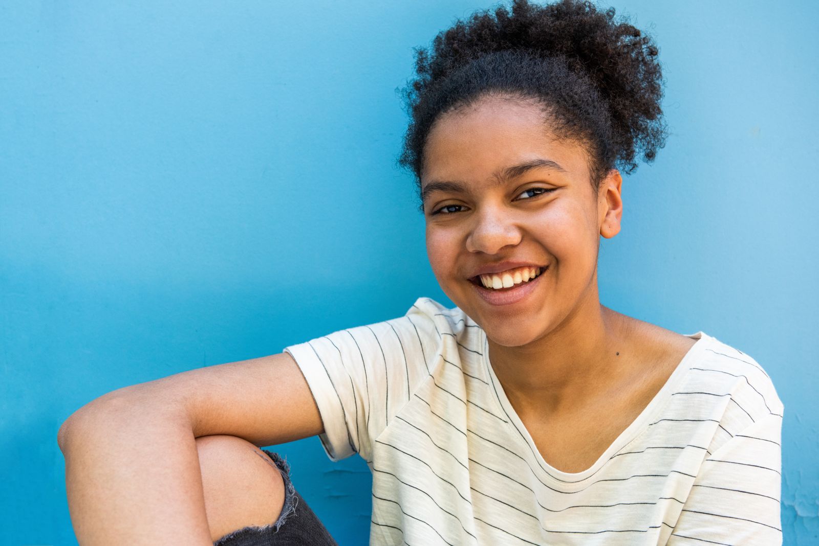 A smiling teenage girl sitting against a blue wall